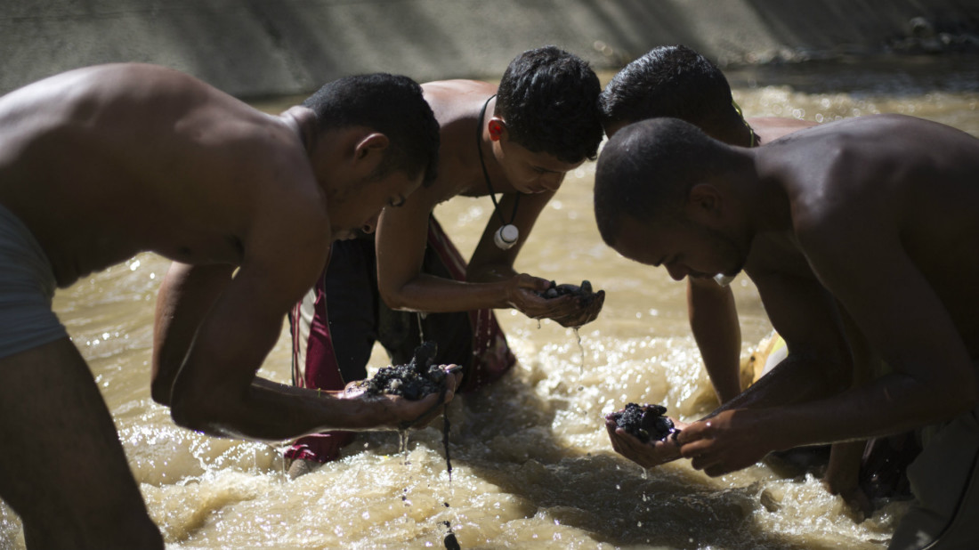 In this Dec. 5, 2017 photo, Angel Villanueva, right, looks for pieces of gold and other valuables in the debris he scooped up from the bottom of the polluted Guaire River, alongside other scavengers, in Caracas, Venezuela. As the 25-year-old scavenges alongside his friends, he's mindful that flash flooding leaves just minutes to get out, or be washed away to his death. Villanueva said he buys food with the money he earns that comes from selling what he finds in the river. (AP Photo/Ariana Cubillos)